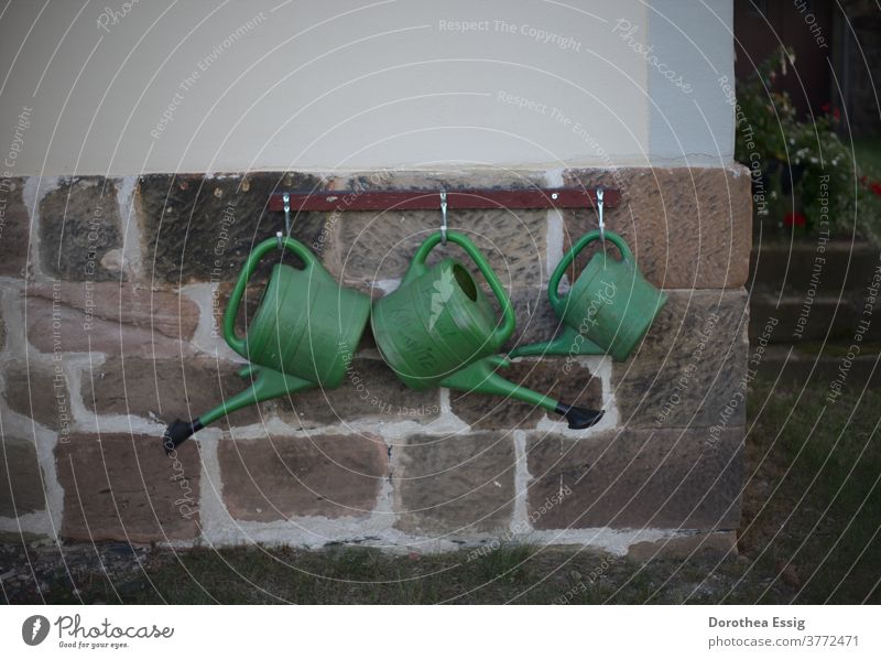 Three watering cans on church wall Watering can Suspended Cemetery Cast Day Green Colour photo Exterior shot Plastic Jug