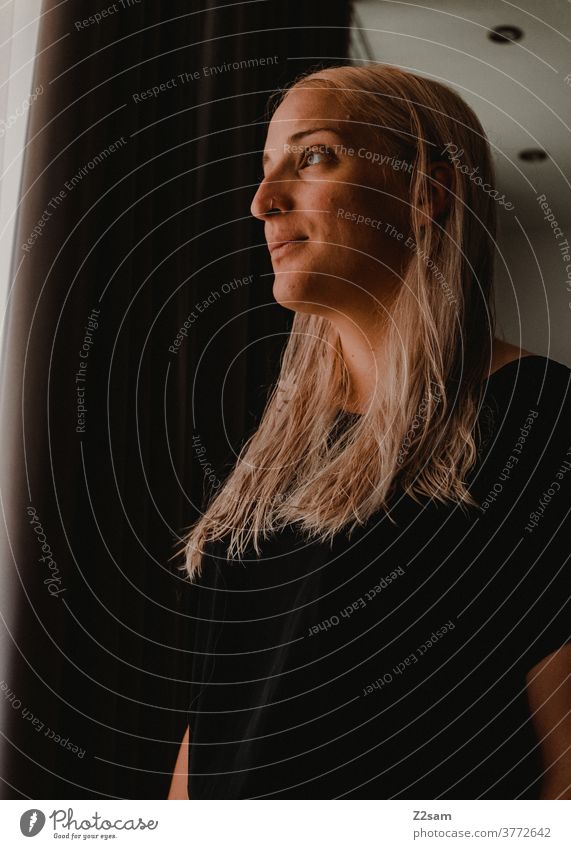 Young woman looks out the window Blonde long hairs Black Drape portrait Face Athletic Looking daylight naturally Beauty & Beauty Self-confident Intensive