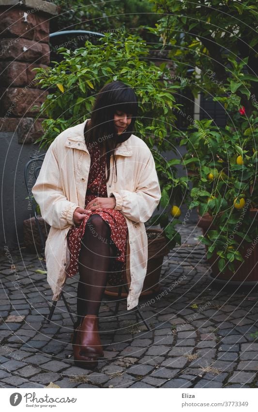 Dark-haired woman in autumnal clothing sitting on a chair outside in the yard and looking to the side Woman Courtyard Autumnal Dress Long-haired