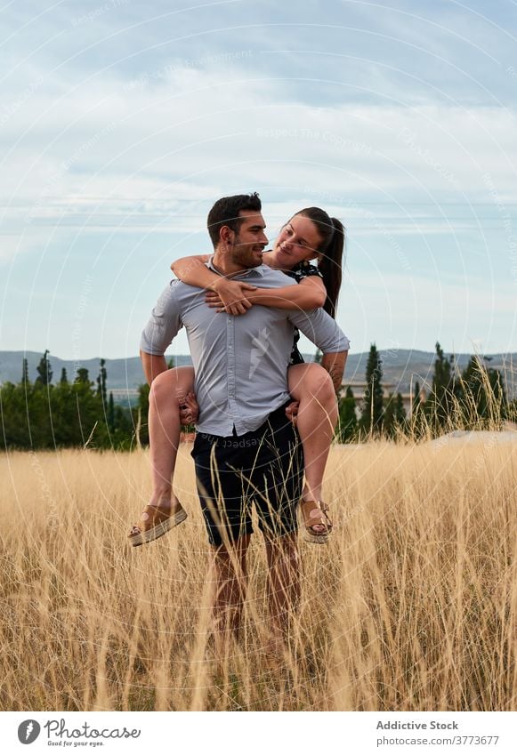 Happy couple cuddling in field in summer piggyback ride love tender relationship meadow weekend countryside happy dried nature cheerful smile rest joy delight
