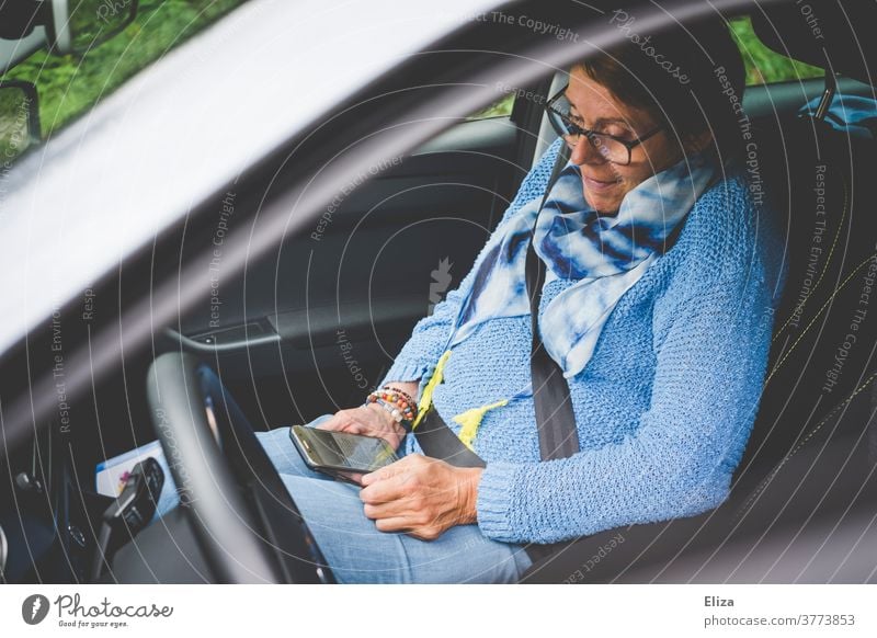 A woman sits in the passenger seat of a car and looks at her smartphone mobile Woman Sit using employed smile Telephone mobile phone Technology