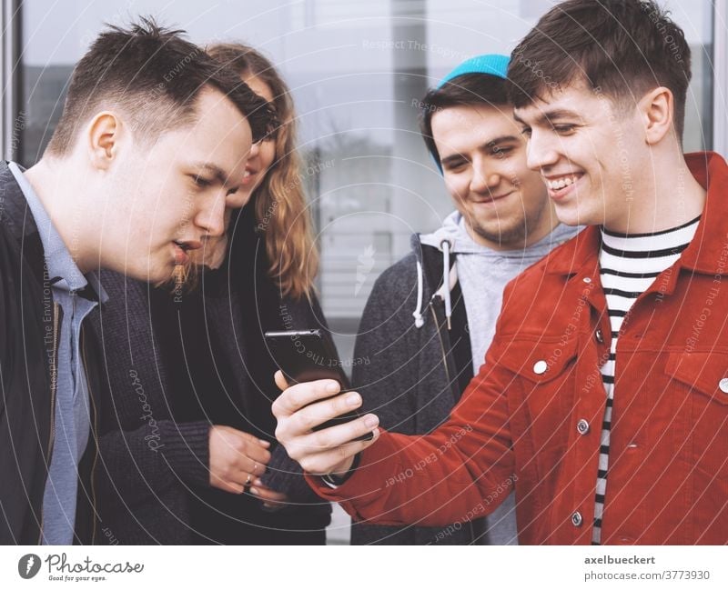 young man showing something funny on his smartphone to a group of teenage friends real people lifestyle mobile cell conversation candid authentic friendship