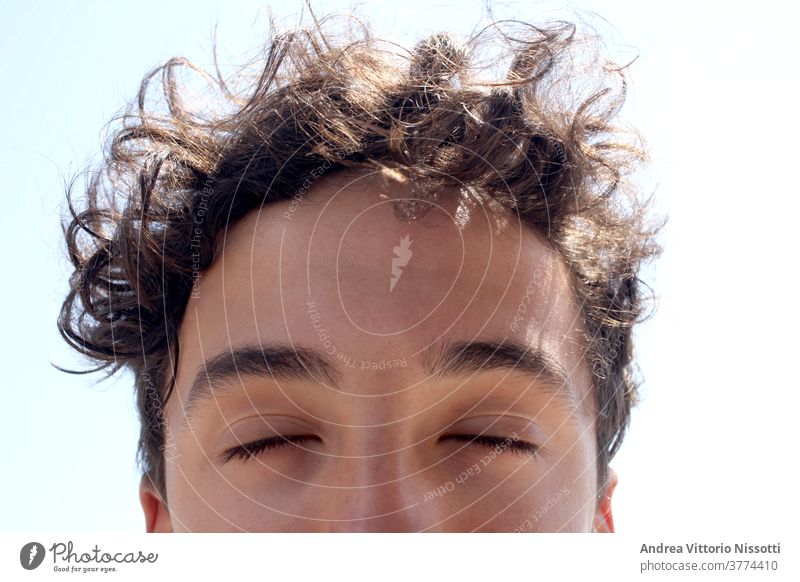 close up on a male teenager with closed eyes face outdoor sunny hair curly horizontal color image boy relax dreaming portrai sky imagin caucasian handsome