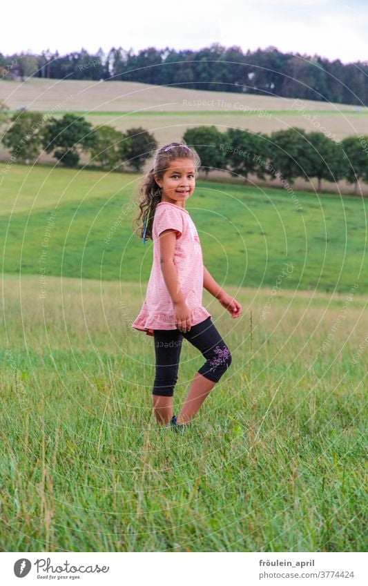 Girls in the country Child long hairs Meadow Green trees Nature Environment Smiling Happiness cheerful Pink Black Field Summer Infancy Joy Exterior shot Grass
