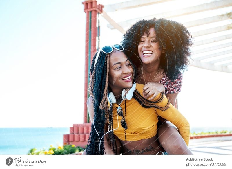 Black female friends having fun on embankment in summer piggyback women delight weekend best friend promenade ethnic black african american braid curly hair