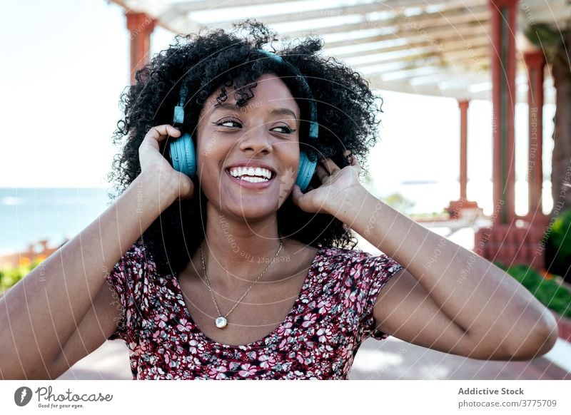 Smiling black woman enjoying music on promenade wireless headphones listen delight carefree summer female ethnic african american curly hair afro hairstyle