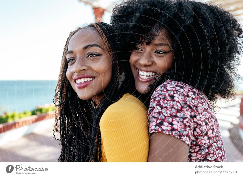 Cheerful ethnic women hugging at seafront best friend friendship together delight summer embankment black african american braid curly hair hairstyle cheerful