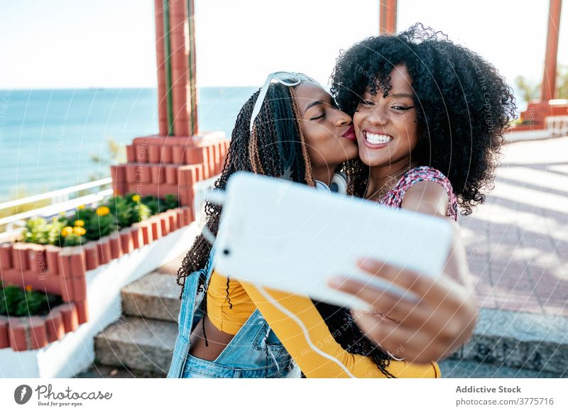 Cheerful black friends taking selfie in city hug smartphone women friendship cheerful bonding using summer promenade ethnic african american braid curly hair