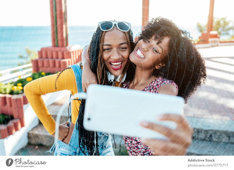 Cheerful black friends taking selfie in city hug smartphone women friendship cheerful bonding using summer promenade ethnic african american braid curly hair