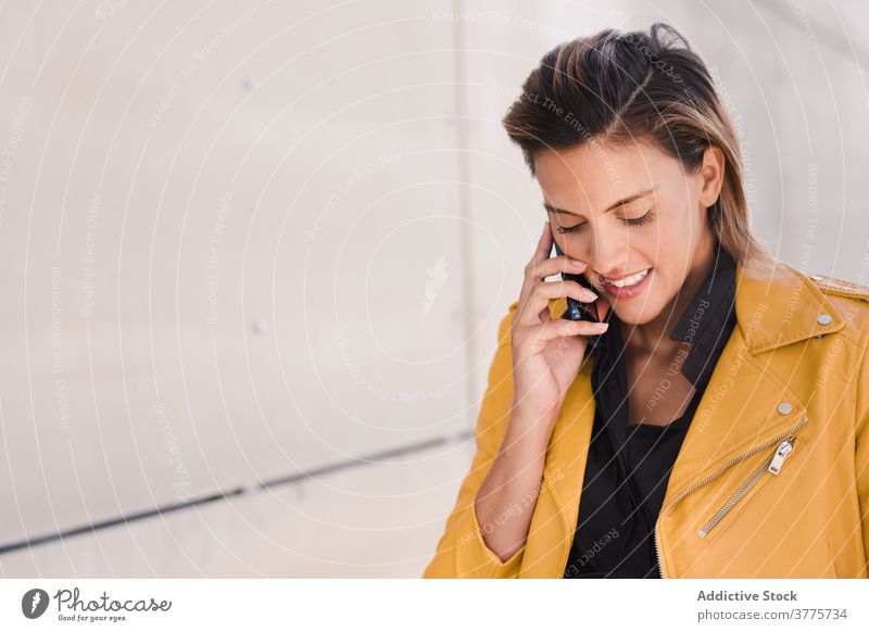 Smiling woman speaking on smartphone near building talk call city cellphone conversation using style female content gadget device communicate modern urban