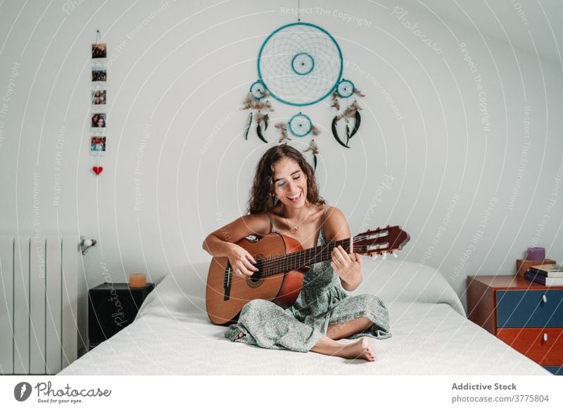 Positive woman playing guitar in bedroom guitarist music cheerful laugh talent entertain carefree instrument female ethnic acoustic cozy home happy musician
