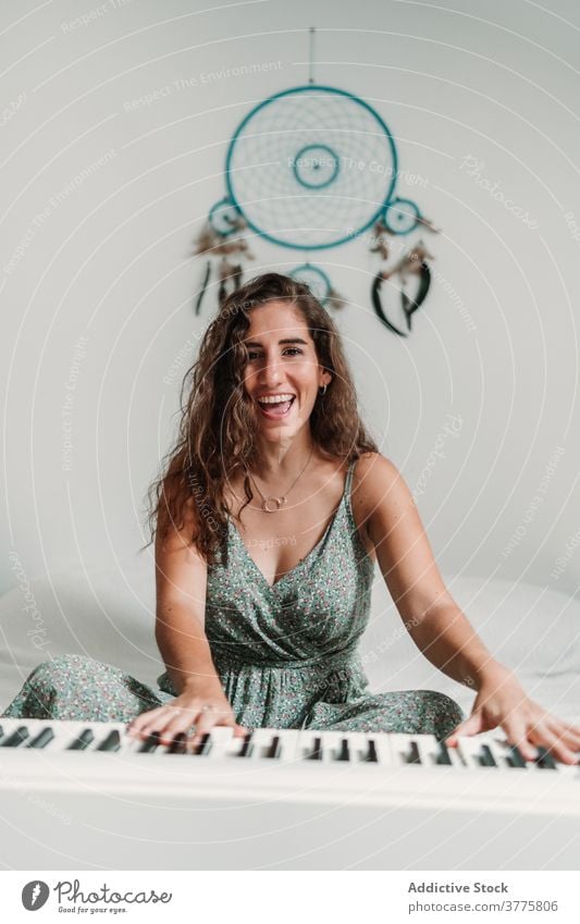 Smiling woman playing piano in living room music musician rehearsal talent skill creative melody ethnic female modern apartment song perform sound entertain sit