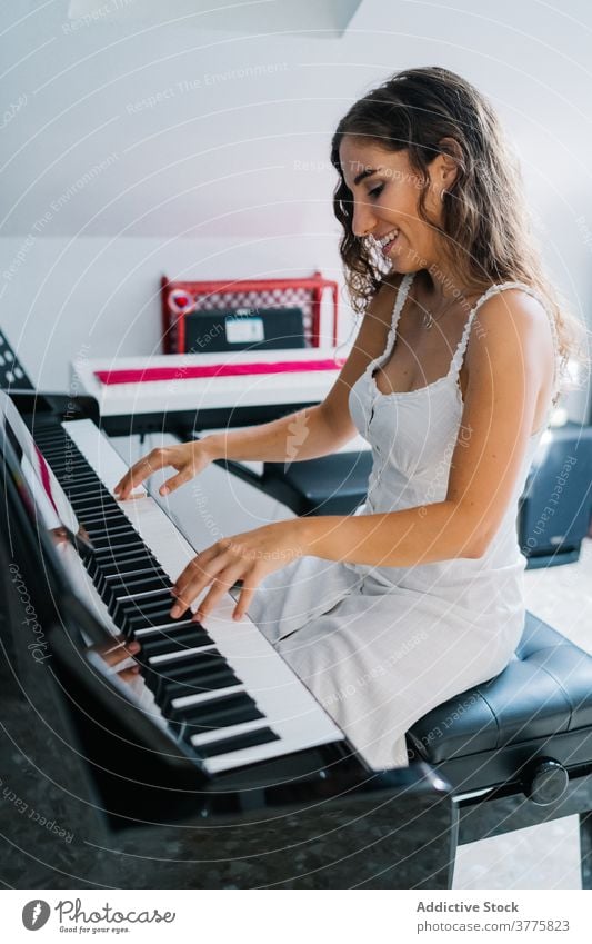 Smiling woman playing piano in living room music musician rehearsal talent skill creative melody ethnic female modern apartment song perform sound entertain sit