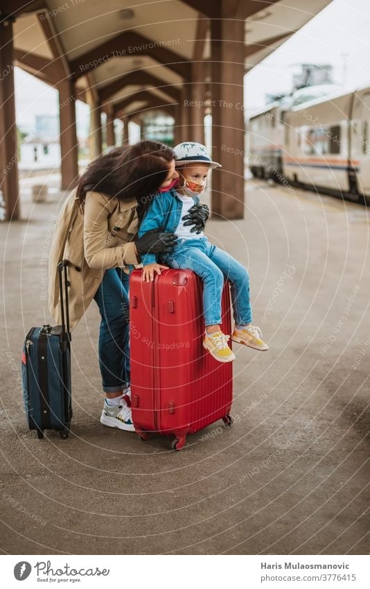 Mother and child with face mask and luggage bags waiting on train station adult baggage beautiful caucasian city corona virus covid travel covid-19 destination
