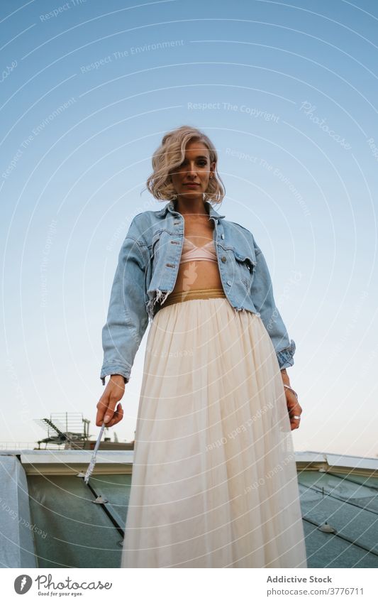 Calm woman in stylish wear on rooftop sunset relax tranquil building cityscape old shabby female skirt denim jacket chiffon tulle sundown sky casual style calm
