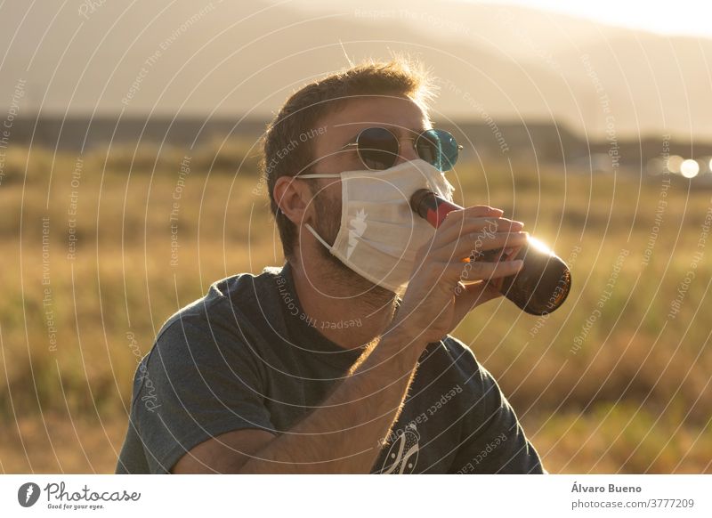 Young man tries to drink beer wearing a protective face mask. day sunset daylight one person young adult sunglasses outdoors landscape natural environment