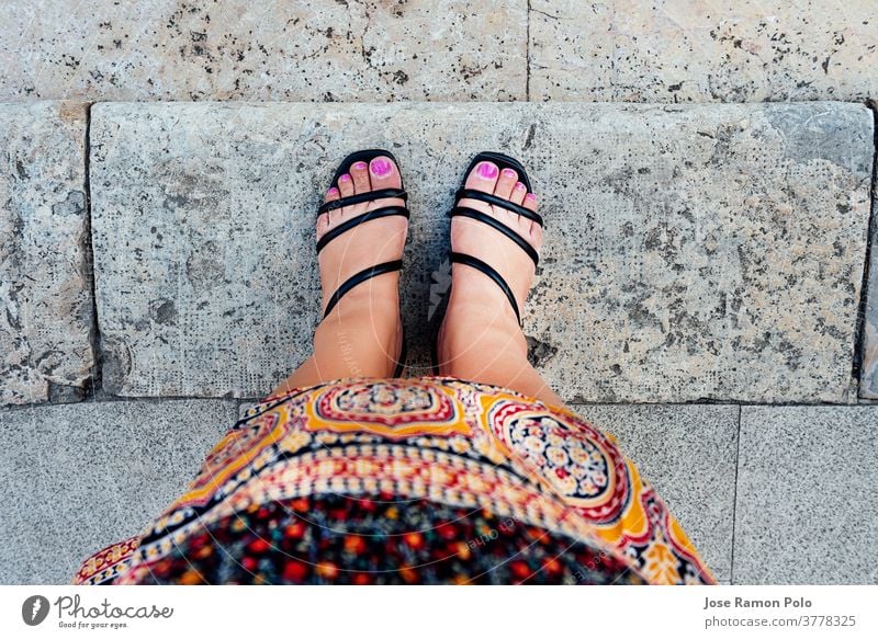 woman's feet in first person view with fuchsia painted nails and black shoes, in Moroccan tribal dress, on gray stone tiles. ethnicity concept people foot
