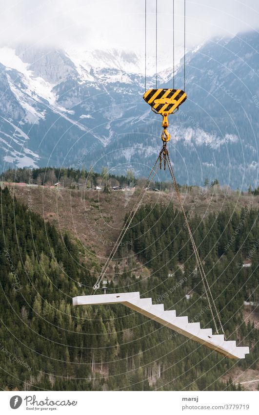 Floating concrete career stairs on crane hook, presented in front of snow-covered mountains hanged Chain suspension Hang Stairs finished concrete element
