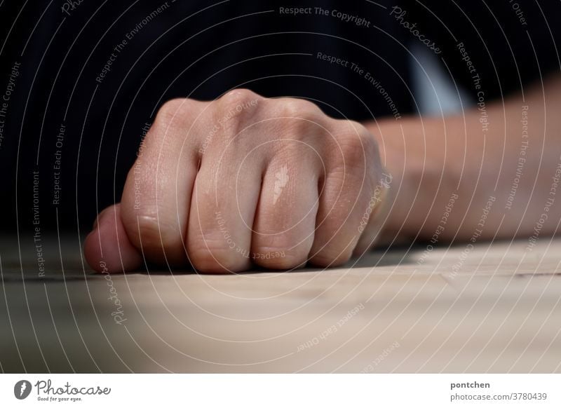 A clenched fist on a table. Anger, aggression. Fist by hand Table furious Aggression Force Aggravation sensation Fingers Woman Hatred arm Impatience nervous