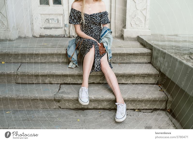 Faceless shot of young slim woman sitting on stairs outdoors holding camera in her hands long female legs day city hipster fashion summer urban shoes stylish