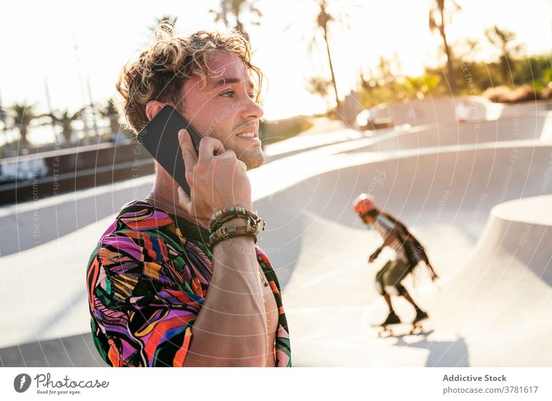 Cheerful hipster talking on smartphone in skatepark skater man style trendy communicate call activity ramp young male lifestyle modern millennial funky active