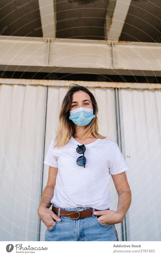 Female teenager in protective mask standing against metal wall woman covid coronavirus urban new normal serious alternative modern female student millennial