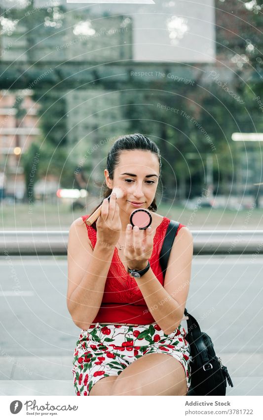 Young woman with mirror applying blush on street makeup beauty cosmetic urban modern young female brunette glamour style fashion lifestyle contemporary feminine