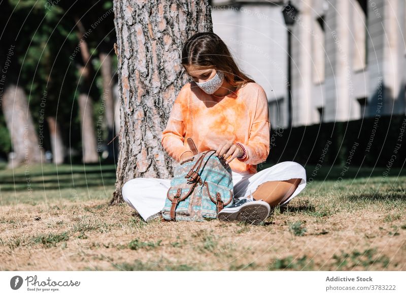 Young woman in mask looking inside bag near tree student sit rummage lawn university pandemic female madrid spain search college covid 19 covid19 coronavirus