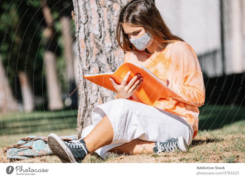 Female student in mask reading near tree woman university notebook homework education pandemic street study female exam prepare learn madrid spain campus young