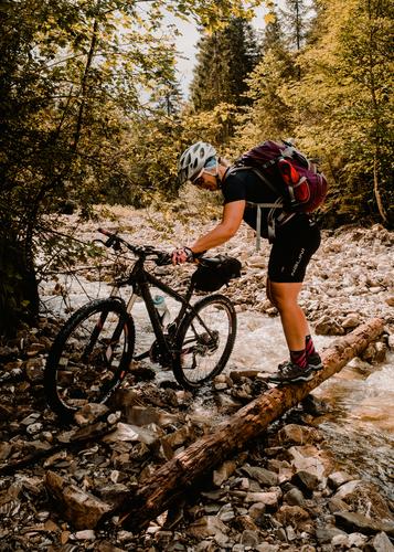 Young woman crosses river creek with her mountain bike Mountain bike mtb Bicycle Adventure Brook River Traverse Push stones Forest Alps mountains Nature