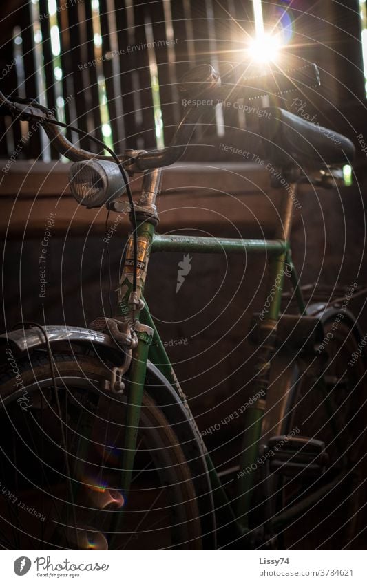 Old, green men's bicycle on the barn floor, illuminated by the sun's rays penetrating from outside between the wooden boards Bicycle Retro barn find Flea market