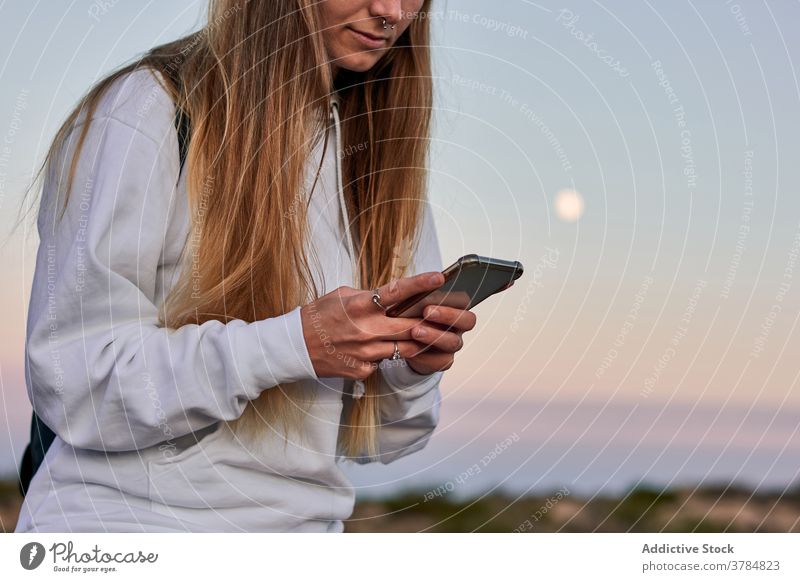 Peaceful woman browsing smartphone on promenade at sunset travel using twilight relax embankment female fence wooden surfing traveler calm internet vacation