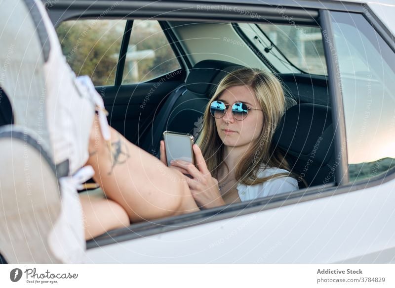 Tranquil woman using smartphone in car relax road trip adventure wanderlust carefree freedom female backseat traveler rest holiday device window cellphone
