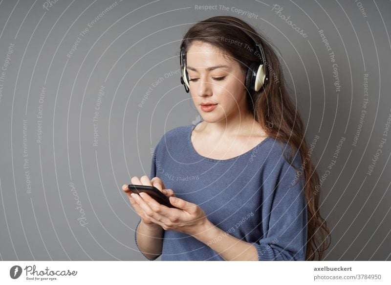 young woman listening to music with wireless bluetooth headphones and mobile smart phone smartphone cordless cell girl female person people caucasian attractive