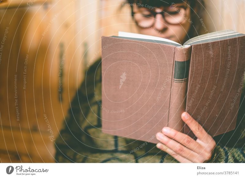 A woman with glasses is reading a book at home Reading Book Eyeglasses Bookworm Cozy Reading matter Novel Education Literature hollowed concentrated Sweater