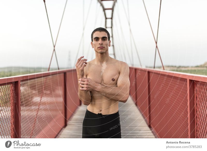 Stretching man on pedestrian bridge portrait run runner strong fit fitness red footbridge footpath men male young adult one person torso muscular muscle