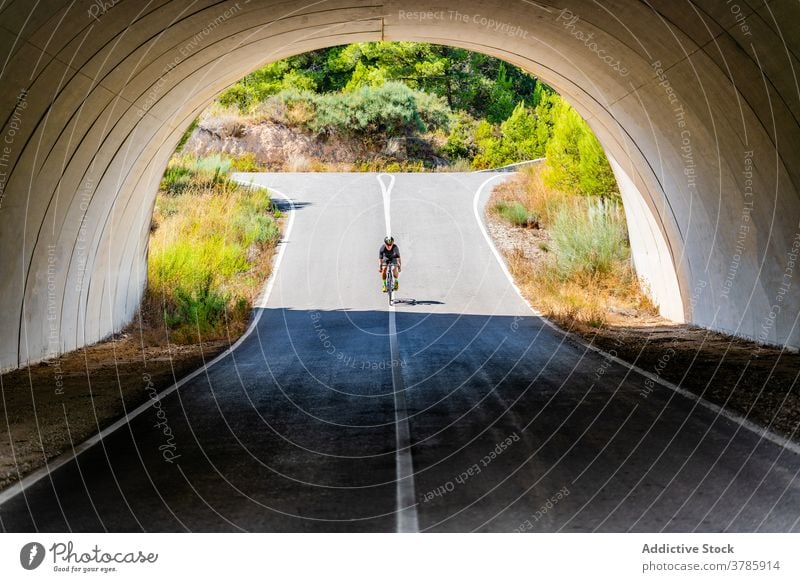 Cyclist riding bike under bridge in countryside cyclist ride road man arch bicycle active lifestyle sport activity healthy summer viaduct archway roadway