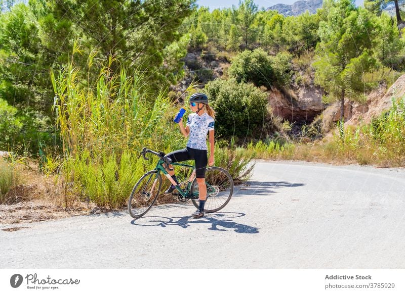 Cyclist drinking water during ride training in mountains cyclist bike rest refresh thirst sport activity woman tired break recreation wellbeing vitality bicycle