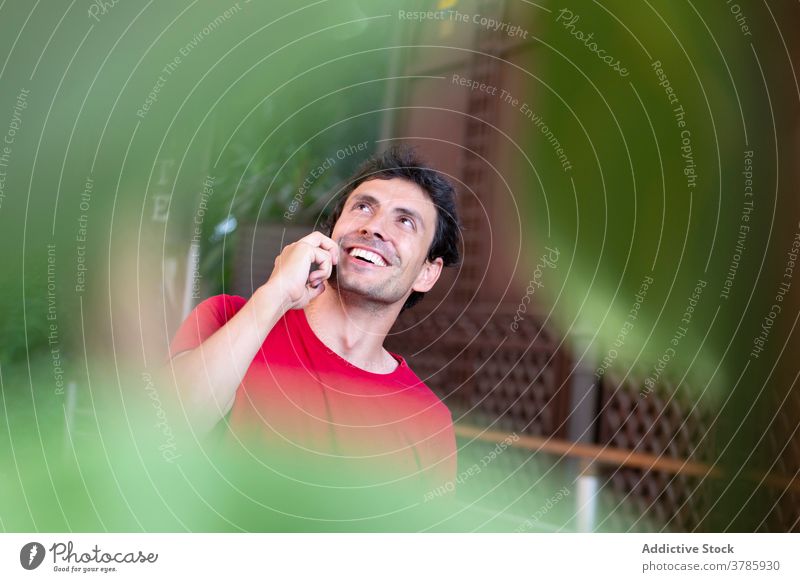 Positive young man with red t-shirt making a call and smiling station smartphone lifestyle speaking entrepreneur public urban caucasian modern passenger plants