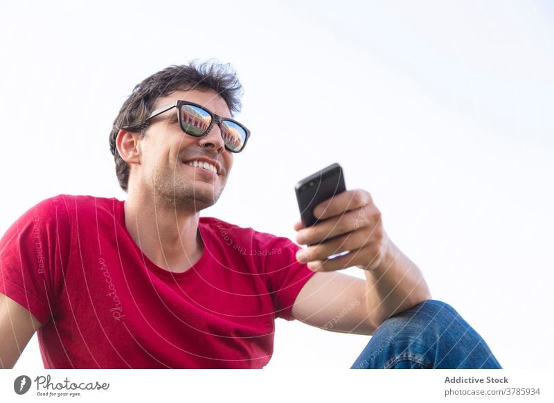 Positive young man in the park with sunglasses and smartphone happiness smile sky positive lifestyle relax outdoor person joy grass male freedom people concept
