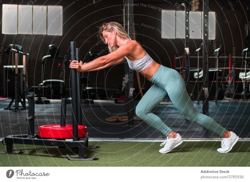 Muscular woman pushing sled in gym weight sledge workout heavy equipment exercise strong muscular female sportswoman fit metal intense wellness physical fitness