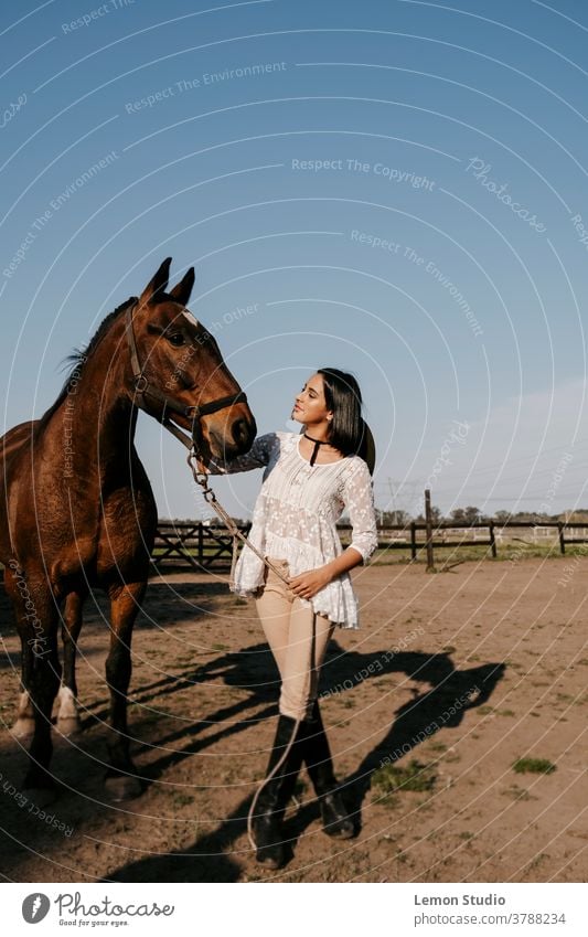 Latin woman touching a brown horse's head latina caressing free air field grass green sky blue trees vertical patagonia spring riding day animal horizontal