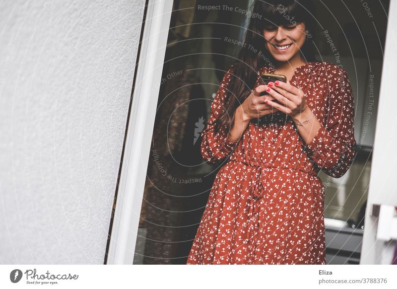 Young woman in red dress with white pattern types smile into her smartphone Woman smilingly using Modern Dress Red at home Joy Laughter Cellphone Telephone