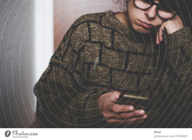 A woman with glasses looks bored into her cell phone Cellphone Exasperated Woman Boredom Face Sadness smartphone mobile phone Reading Youth (Young adults)