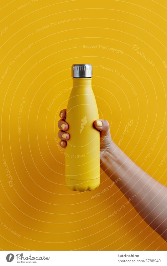 Close up of female hand, holding yellow reusable steel bottle on yellow background monochrome ecologic water thermo bright mockup woman faceless aluminum blank