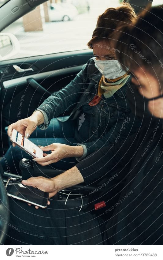Man and woman sitting in a car using smartphones wearing the face masks to avoid virus infection caucasian covid-19 lifestyle outbreak outdoors pandemic