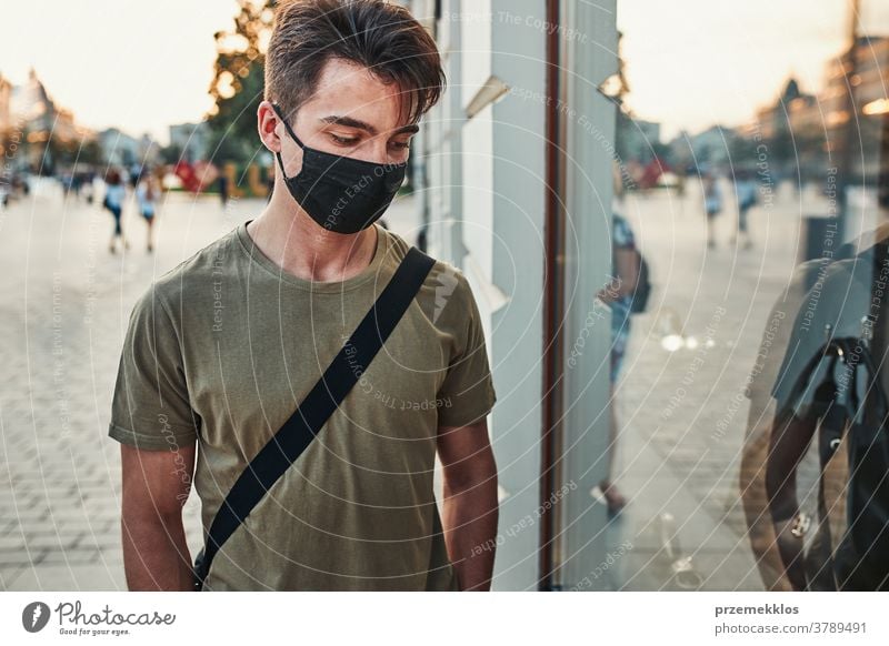 Young man walking along a store front in the city center wearing the face mask to avoid virus infection caucasian conversation covid-19 lifestyle outbreak