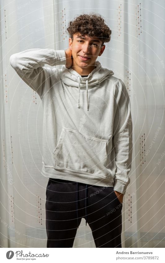 Attractive young man with curly hair wearing white sweatshirt posing on white curtains background cheerful casual smile male adult handsome happy attractive