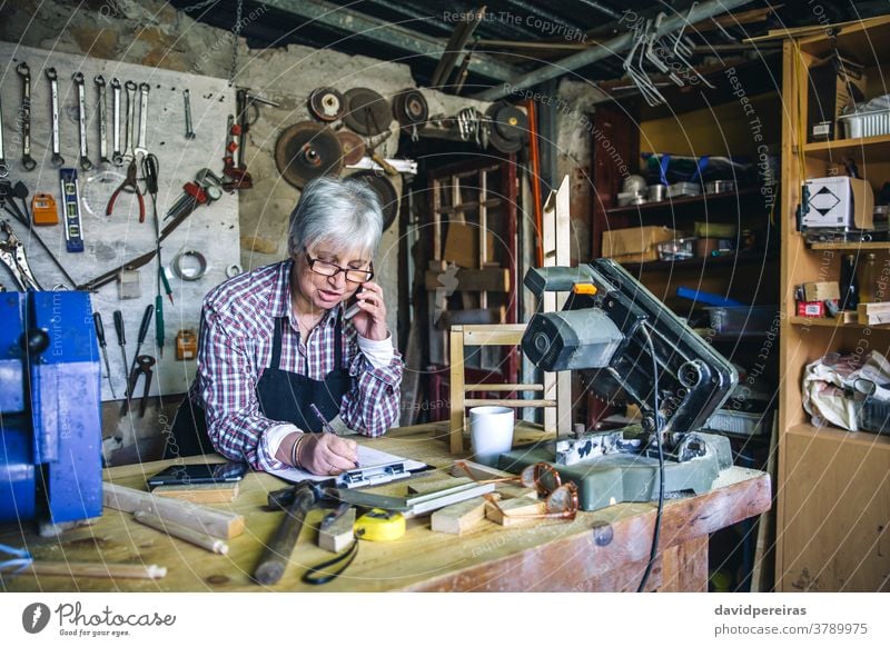 Female carpenter in her workshop carpentry woman senior talking mobile cell phone custom made business mature writing wood people old caucasian artisan aged