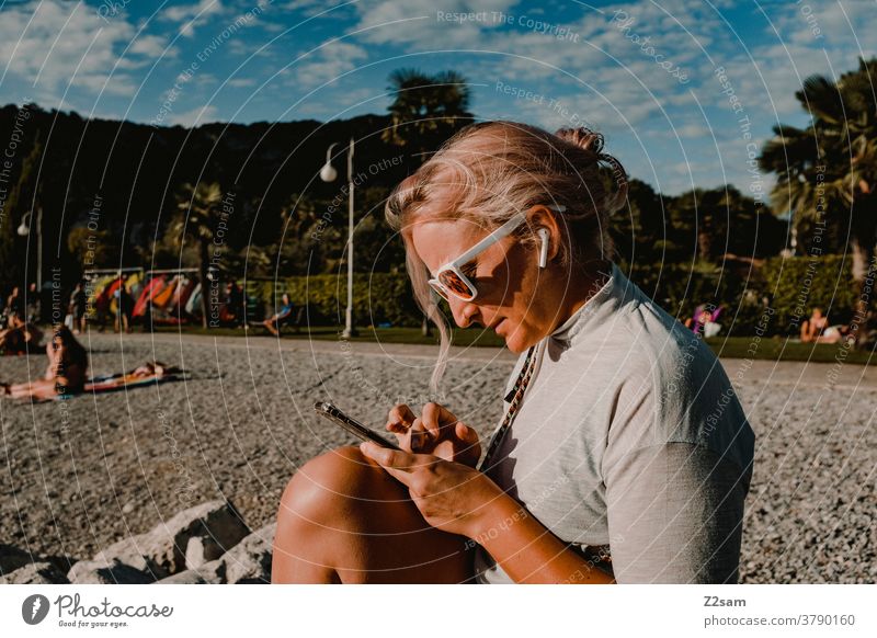 Junge Frau mit Smartphone am Strand von Torbole | Gardasee gardasee torbole junge frau blond lange haare sonnebrille musik hören telefon smartphone handy strand